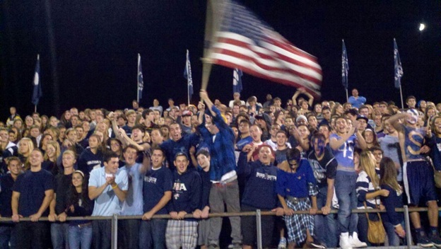 MiddSouth+Nation+cheers+on+the+team+during+a+blue-out+on+9%2F21+vs+Howell%2C+led+by+flag+bearer+Kieran+Campbell.